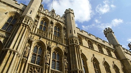 crenelated façade of a stone Cambridge building under a partially cloudy sky